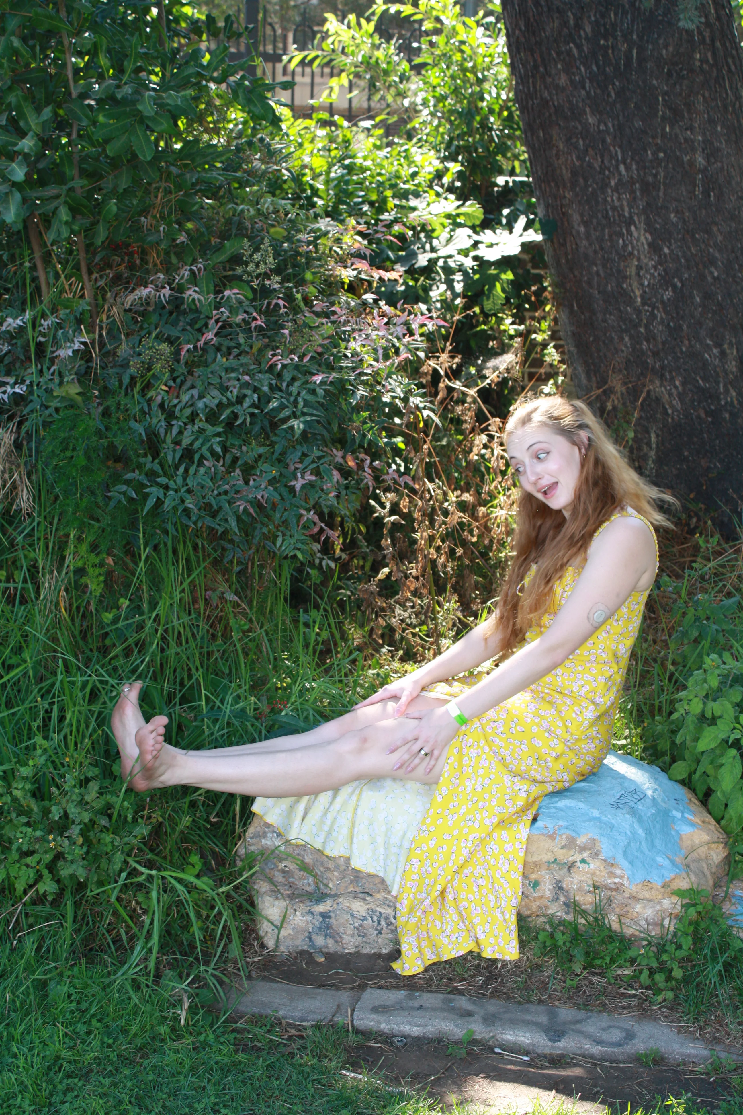 Jordie Morris stretching her legs while seated on a blue-painted rock at the Exposition Park Rose Garden.